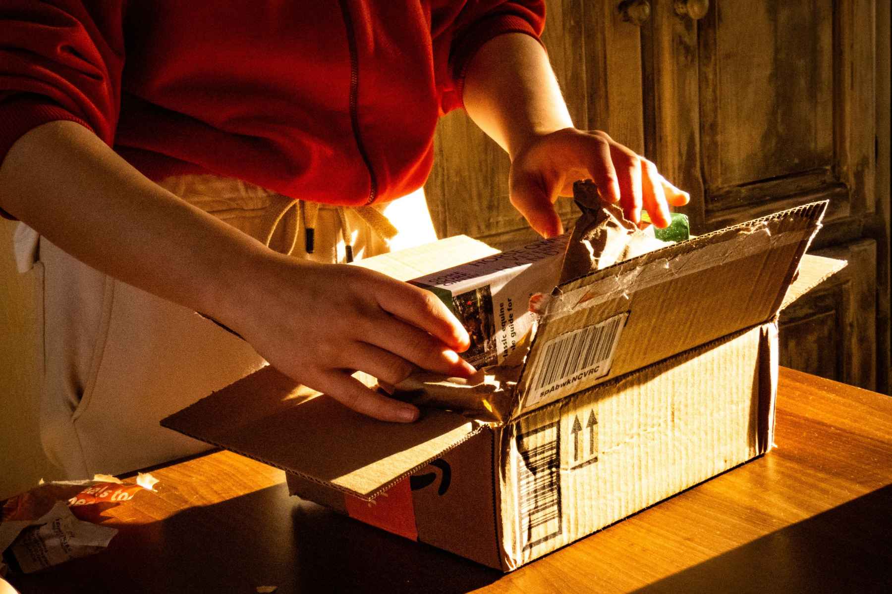A woman opens a plain cardboard box on her kitchen counter to test a new product.